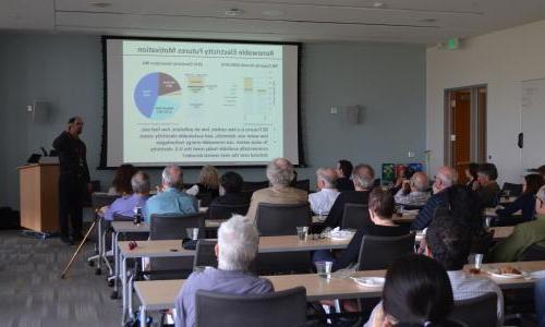 People sit in a room watching a presentation on renewable electricity. 